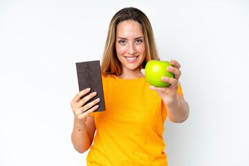 Young caucasian woman isolated on white background taking a chocolate tablet in one hand and an apple in the other