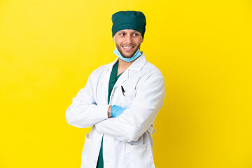 Surgeon blonde man in green uniform isolated on yellow background with arms crossed and happy