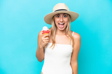 Young caucasian woman in swimsuit with a cornet ice cream isolated on blue background with surprise...