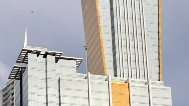 Panning Two People From A Distance In Jumpsuits As They Soar Across A City Sky - Panama City, Panama
