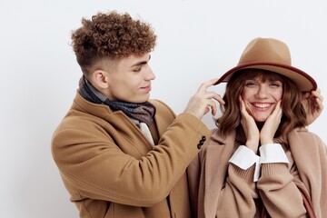 a close horizontal photo of a happy couple in stylish autumn clothes, a woman stands holding a bag in her hand, and a man adjusts her hat looking cute with love