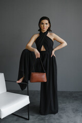 Beautiful woman in black holds fashion handbag posing at studio. Girl model posing. Fashionable person.Beautiful woman in black holds fashion handbag posing at studio.