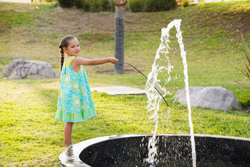 Niña feliz hermosa jugando y divertida con la fuente de agua en el parque al aire libre en un...