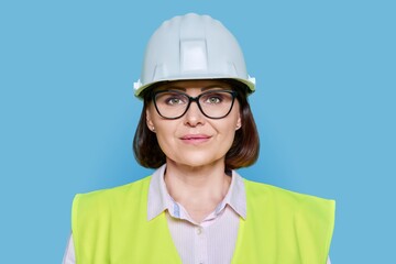 Female industrial worker in protective hard hat and vest on blue background