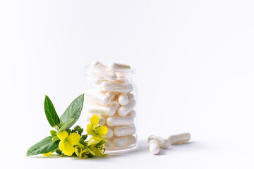 White medical capsules in a glass bottle on white background with fresh flowers and leaves. Natural...