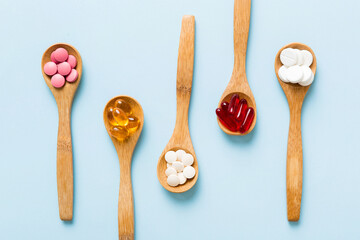Vitamin capsules in a spoon on a colored background. Pills served as a healthy meal. Red soft gel vitamin supplement capsules on spoon