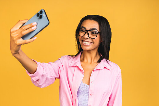 Young funny african american black casual woman grimacing and making selfie on smartphone isolated over yellow background.