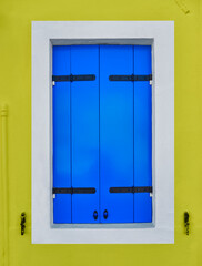 Ventana de madera azul ,con marco blanco y fachada amarillo limón
