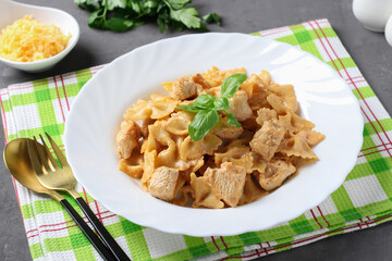 Pasta farfalle with turkey in tomato-sour cream sauce, served cheese and basil on gray background