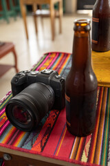 table with colorful tablecloth with a digital professional camera next to a bottle of beer, refreshing drink and technology, hobby tool, lifestyle