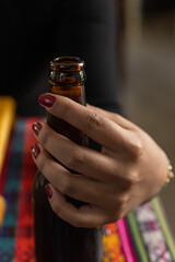 hand with red nails holding a glass bottle, drink and lifestyle, studio with colorful tablecloth, texture details