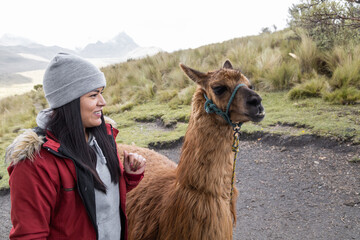 lifestyle in the countryside with a young woman wearing warm clothes next to a llama, domestic animal, scene with nature in the day