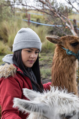 beautiful young woman wearing a wool cap and jacket next to a llama, domestic animal, scene with nature, farm lifestyle
