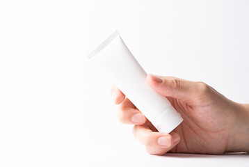 Womans hand holding white unbranded container with cosmetic product such as cream, balm, lotion or toothpaste on white background close up. Skin care concept.