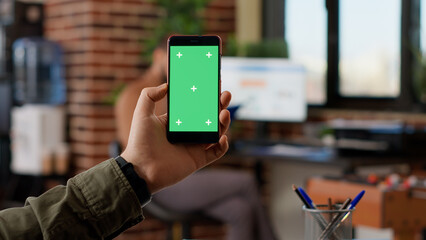 Businessman analyzing smartphone with greenscreen display in startup office. Looking at isolated copyspace template with blank mockup chroma key background, digital mobile phone.