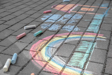 Fototapeta premium Rainbow with grass, house and clouds painted in colored chalk on a path on the street