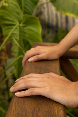 hands of a person approaching a wooden handrail in the background natural leaves of a garden, texture detail, nature wallpaper with part of the body