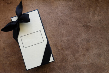 Cream Colored Rectangular Box with Black Ribbon against a Brown Textured Background