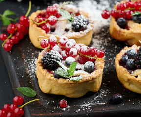 Fruit tart with red currants sprinkled with powdered sugar on a black table - obrazy, fototapety, plakaty