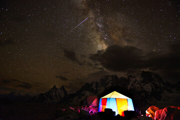 An illuminated tent of trekkers, with the background of Karakoram mountains and milkyway...