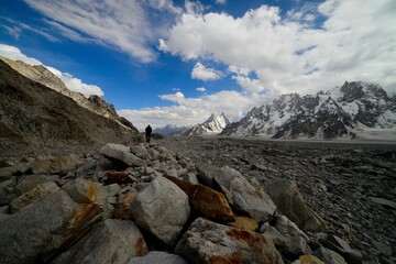 Fototapeta na wymiar A trekker walking on the brink of Biafo glacier in the Karakoram National Park on a beautiful sunny and partly cloudy day. 