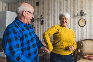 Joyful caucasian elderly woman dancing with her happy husband together in the living room of their...