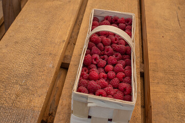 This is a basket with raspberries on a wooden background.