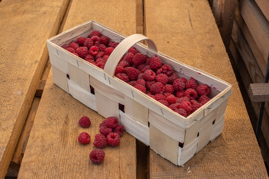 This is a basket with raspberries on a wooden background.
