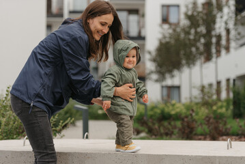 Fototapeta premium A mom is teaching her female toddler how to do steps in the street at noon.