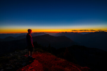 An athletic adventurous male hiker standing on top of a mountain looking out at a beautiful sunset.
