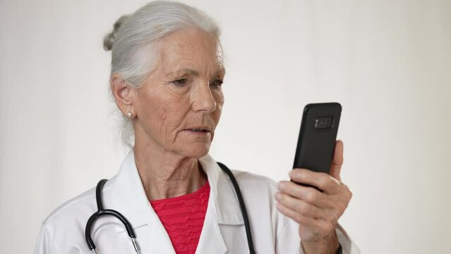 Pretty senior, elderly, mature woman doctor making video call with patient, tele health, telemedicine concept on smartphone