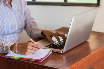 person writing about blank notebook, laptop open on a desk