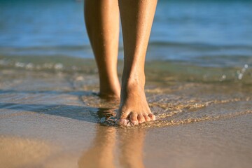 A woman walking on the beach, stepping in the water shore. People in nature.
