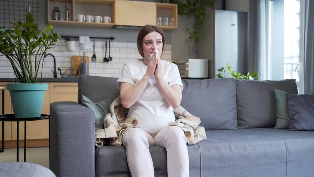 sick pregnant woman with cold cough and temperature blowing nose with runny nose sitting on sofa at home. ailing female got flu during pregnancy. Disease. suffering Allergy cold symptoms