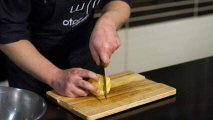 A man cutting a peeled potato on a wooden board. Art. Close up of male chef preparing a dish and using a steel knife for cutting vegetables.