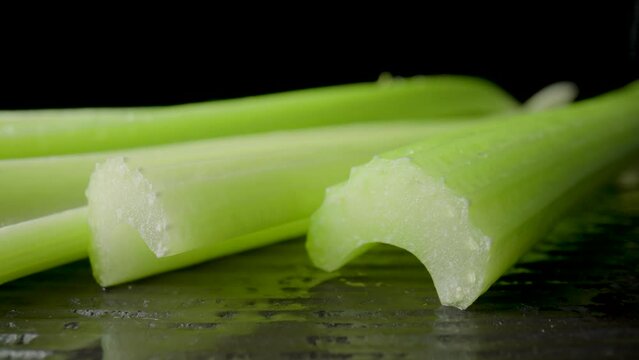 Row of green celery stalks lying on black board on isolated black studio background. Macro shot of fresh celery and green and red hot peppers. Ingredients for salad. Slow motion ready 59.94fps.