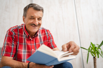One man senior caucasian male with read book at home sitting