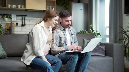 young married couple, pregnant wife and husband use laptop while shopping online sitting at home on sofa in room Choosing goods for newborn child on Internet Family Browsing computer during pregnancy - Powered by Adobe
