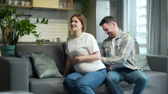 Husband gives pregnant wife back massage during pregnancy sitting on sofa at home. Love care and support of man. Нappy family couple is expecting a baby. Back pain In anticipation of childbirth