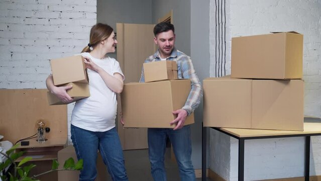 a young pregnant couple with boxes moves into a new apartment. home holding cardboard box. Family expecting baby. House mortgage