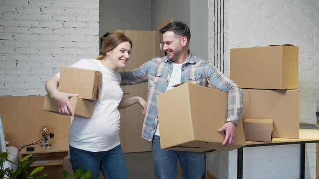 a young pregnant couple with boxes moves into a new apartment. home holding cardboard box. Family expecting baby. House mortgage