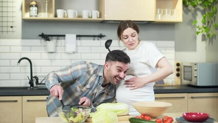 Cheerful happy family couple expecting a baby spend a funny time together in the kitchen at home. A pregnant woman and her husband are dancing and having fun while cooking prepare lunch singing - Powered by Adobe