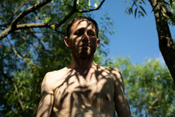 Fototapeta na wymiar Guy in shade of plants without clothes. Man in summer. Wild man.