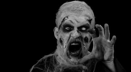 Sinister man with horrible scary Halloween zombie makeup in convulsions making faces, looking...