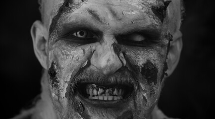 Creepy man close-up face with bloody scars, Halloween stylish zombie makeup. Scary wounded undead guy blows smoke from nose, smiles terribly. Voodoo rituals. Sinister beast, monster, vampire