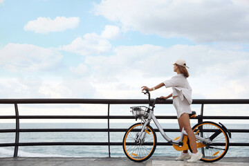 Beautiful young woman with bicycle near sea. Space for text