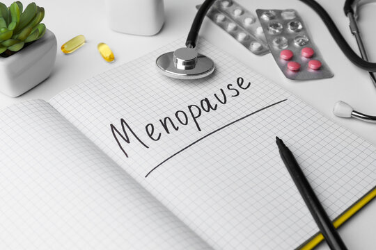 Notebook with word Menopause, stethoscope, pills and houseplant on white background, closeup
