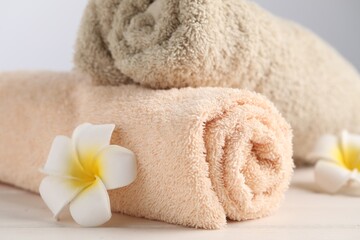 Closeup view of soft folded towels and plumeria flowers on white wooden table