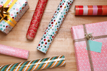 Different colorful wrapping paper rolls and gift boxes on wooden table, flat lay