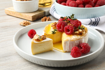 Brie cheese served with raspberries, walnuts and honey on white wooden table, closeup